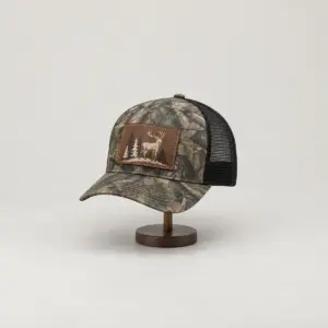 Camo Stag Leather Patch Trucker Cap with artwork on a rectangular Rustic Dark Brown faux leather patch of a stag and three pines in cream and brown, Rec_RDBrown patch, Camo/Black cap, DTF printed on the patch