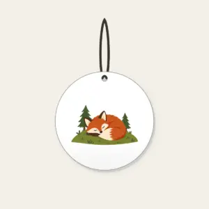 Sleeping Fox on the Hill Ceramic Ornament in white: A rust-colored fox curled asleep on a green hill with two tiny pines.
