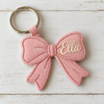 Pink bow-shaped canvas tag embroidered with the name Ella on a keyring