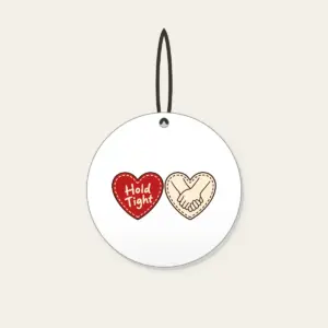 Hold Tight Heart and Hands Ceramic Ornament in white: A red dashed heart marked “Hold Tight” on one side and two clasped cream hands in brown on the other.