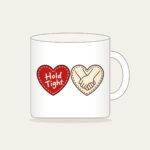 Hold Tight Heart and Hands Mug in white: A red dashed heart marked “Hold Tight” on one side and two clasped cream hands in brown on the other.