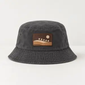 Charcoal Hillside Leather Patch Bucket Hat with patch artwork of a hillside with five small round trees and a sun in cream and tan, DTF printed on a rectangular rustic dark brown faux leather patch, Charcoal hat
