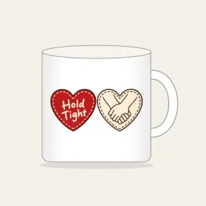 Hold Tight Heart and Hands Mug in white: A red dashed heart marked “Hold Tight” on one side and two clasped cream hands in brown on the other.