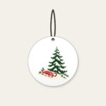 Red Sled on a Snowy Hill Ceramic Ornament in white: A small red sled on a snowy hill beside a tall pine in cream, red and green.