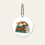 Cat Napping on Three Books Ceramic Ornament in white: A cat curled up asleep on a stack of three books, in warm brown and teal.