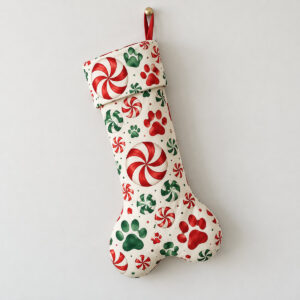 Paw and Peppermint Dog Bone Stocking with peppermint swirls and paw prints in red, white and green across a cream stocking shape with a printed cuff
