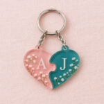 Two linked acrylic heart keychain pieces in rose and teal with initials A and J