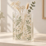 Shelf Garden Acrylic Book Vase with spine and face printed with a pattern of fine ferns and small blossoms in sage and cream on a frosted finish, with three simple dried stems added for photography only