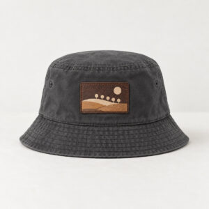 Charcoal Hillside Leather Patch Bucket Hat with patch artwork of a hillside with five small round trees and a sun in cream and tan, DTF printed on a rectangular rustic dark brown faux leather patch, Charcoal hat